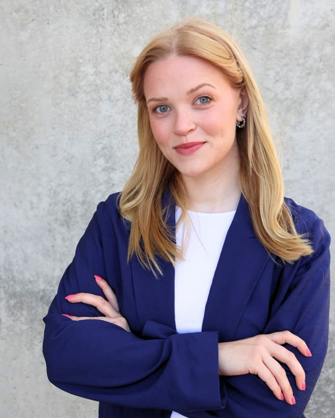 Hilke Terhalle im blauen Blazer vor einer Betonwand, die Arme verschränkt, lächelt in die Kamera.