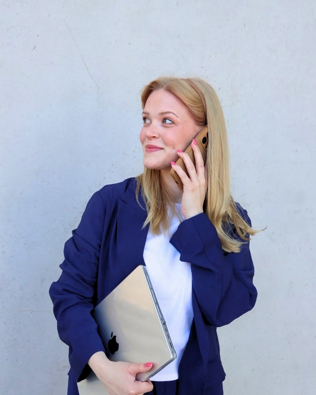Hilke Terhalle im blauen Blazer vor einer Betonwand, telefoniert und hält einen Laptop unter dem Arm.
